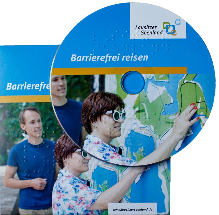 CD-Hülle auf der eine CD liegt: Label "Barrierefrei reisen" zeigt Frau mit Brille, die Landkarte ertastet