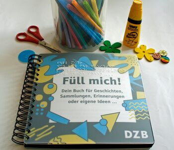 Cover des Ringbuches "Füll mich", oben eine Schere, Filzstifte, Klebstift und kleine, bunte Holzblumen und Holzknöpfe