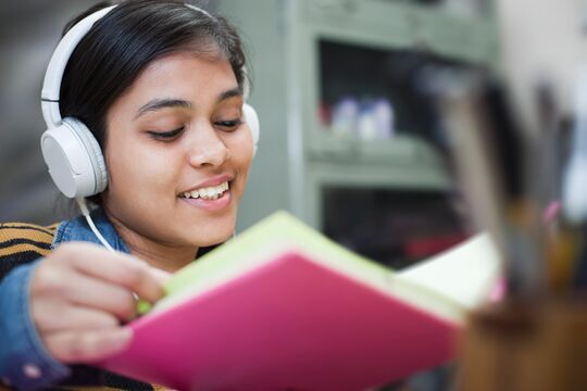 Lächelndes Mädchen mit Kopfhörern und aufgeschlagenem Buch