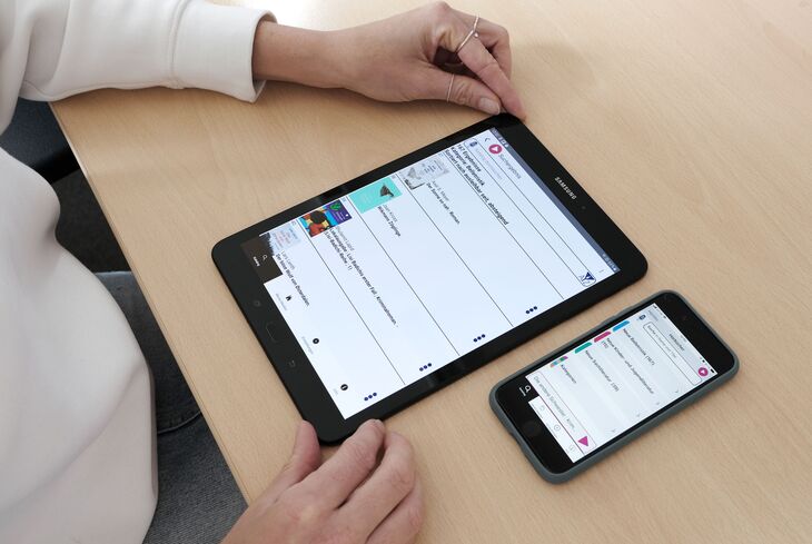 Ein Tablet und ein Smartphone liegen auf einem Tisch. Zwei Hände umfassen das Tablet.