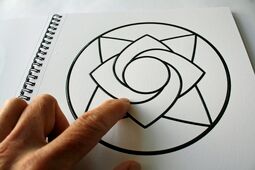 Aufgeschlagenes Ringbuch mit Mandala zum Ausmalen, ein Finger ertastet das Motiv