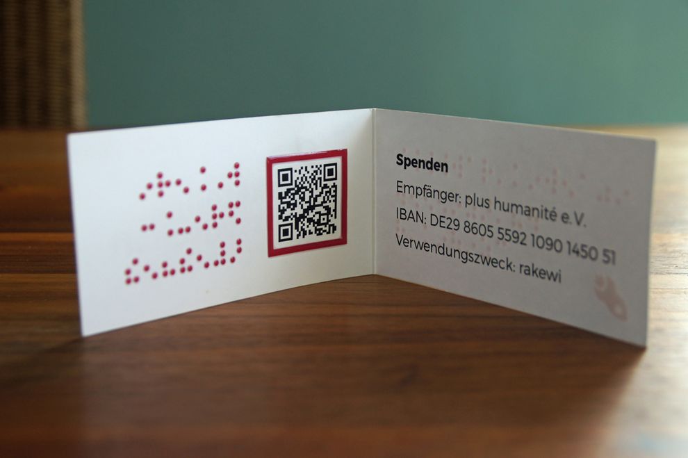 Aufgeklappte Visitenkarte mit rotem Braillelack, Schwarzdruck und QR-Code