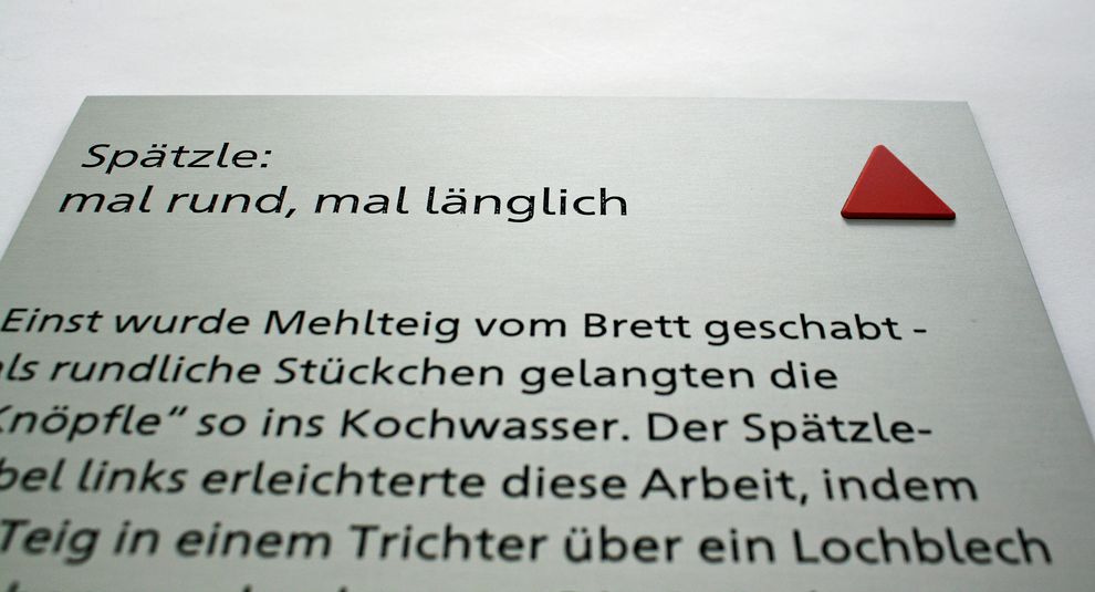 Aluminiumschild Detailansicht mit Text in Schwarzdruck, rechts oben ein rotes taktiles Dreieck