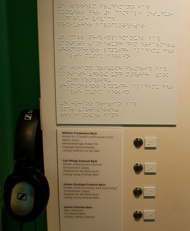 Hörstation: links Kopfhörer, mittig Infotext in Braille, darunter Beschriftung der Knöpfe in Braille